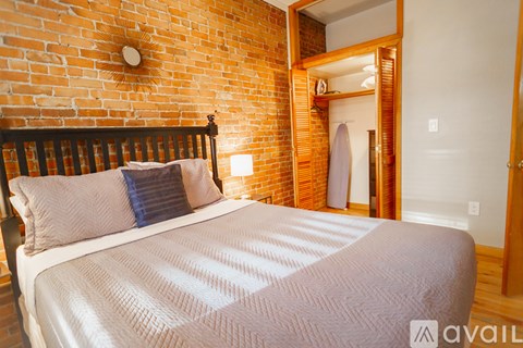 A bed with a white comforter and a blue pillow is in front of a brick wall.