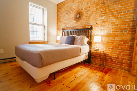 A bedroom with a brick wall and a bed with a white comforter.