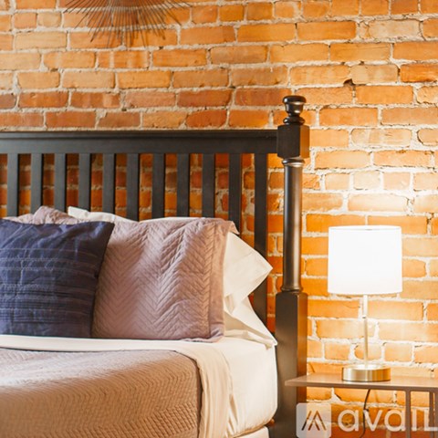 A bed with a white comforter and a blue pillow is in front of a brick wall.