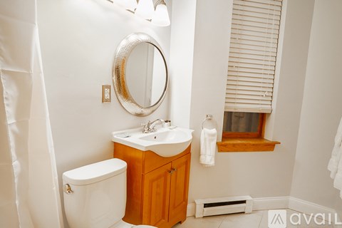 A bathroom with a toilet, sink, mirror, and a window with blinds.