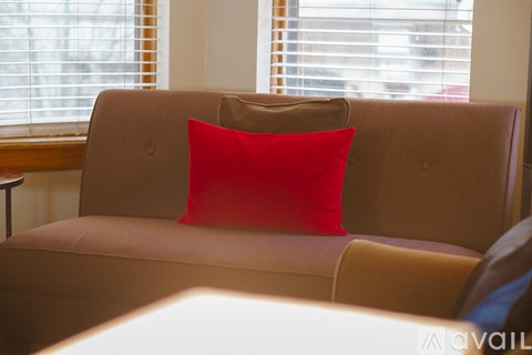 A red pillow on a beige couch in front of a window.
