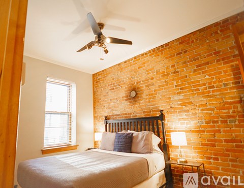 A bedroom with a brick wall and a bed with a white comforter.
