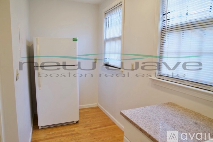 A white refrigerator in a room with a window and wooden floors.