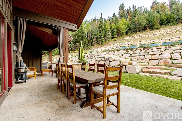 A wooden table and chairs are set up on a patio with a view of a rocky landscape and trees.