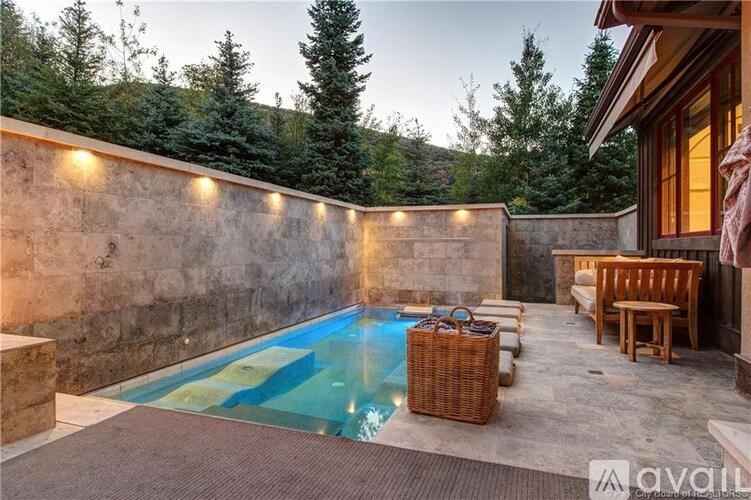 A pool surrounded by a stone wall and wooden furniture.