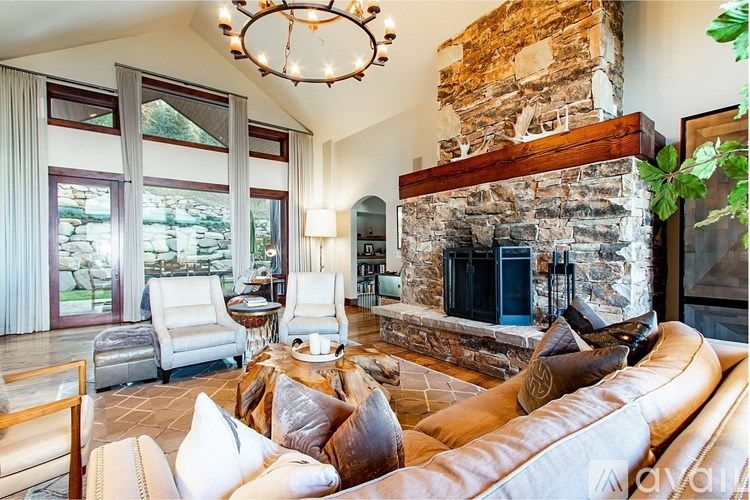 A living room with a stone fireplace and a chandelier.