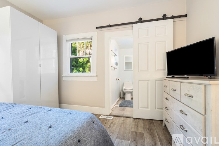 A bed with a white comforter and a pillow with a yellow pillow case sits in a room with a window.