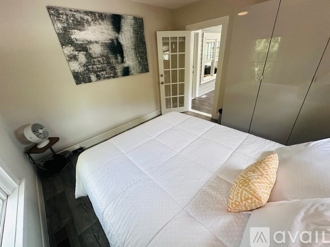 A bedroom with a white bed and a painting on the wall.