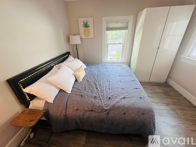 A bedroom with a bed, nightstand, and a window with a pineapple picture.