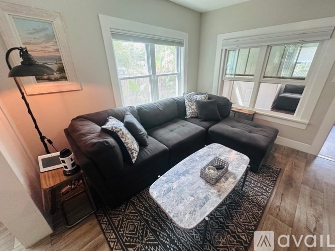 A black couch with a grey pillow and a grey and white coffee table in front of it.