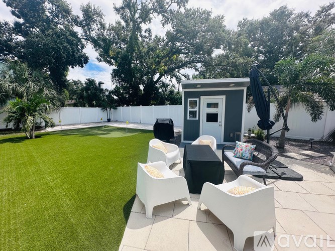 A backyard with a white fence, a small white building, and a black umbrella.