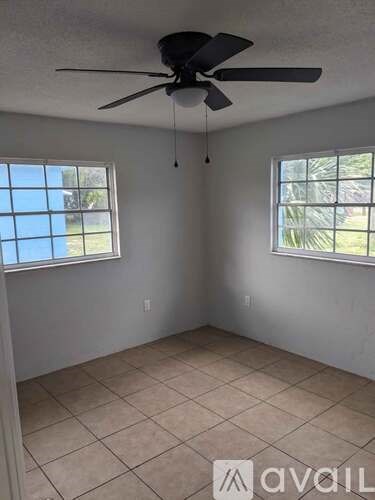 A room with a ceiling fan and two windows.