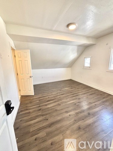 A room with wooden flooring and a door on the left.
