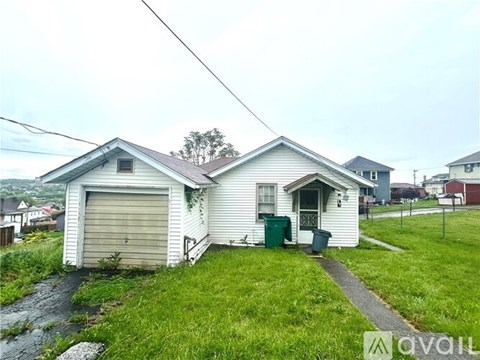 A white house with a grey roof and a green trash bin in front.