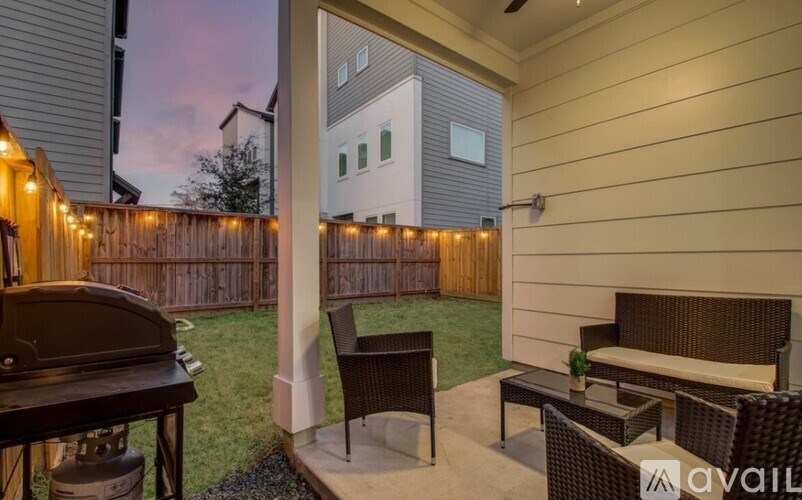 A patio with a table, chairs, and a grill with lights on the fence.