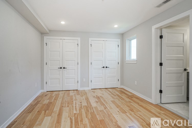 A room with wooden flooring and white walls, with two doors and a window.