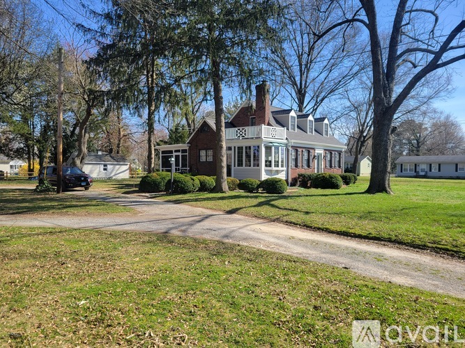 A large house with a red brick chimney is surrounded by trees and a grassy lawn.