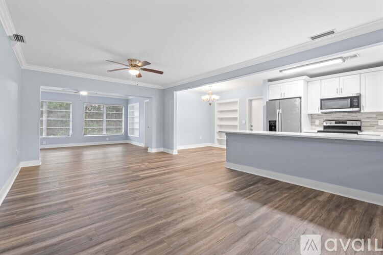 A spacious room with a kitchen in the background and a chandelier hanging from the ceiling.