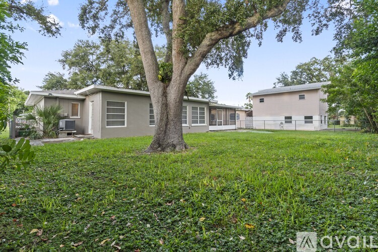 A tree stands in the middle of a grassy area in front of a house.