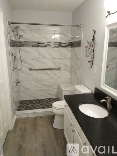 A bathroom with a marble shower and a black counter top.