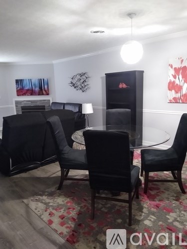 A living room with a black sofa, two chairs and a glass table.