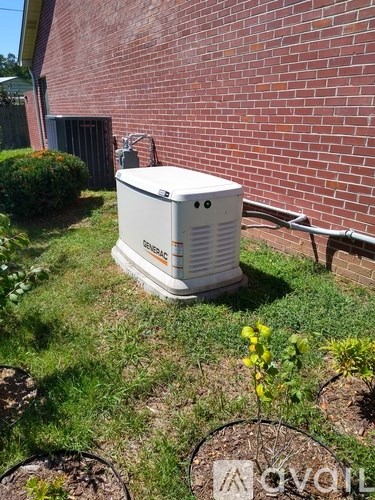 A white air conditioner unit is placed on a grassy area outside a brick building.