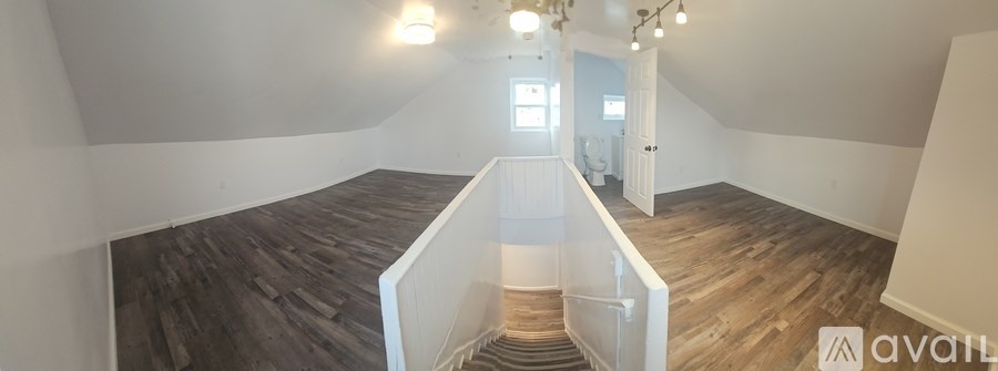 A room with wooden floors and white walls, with a staircase leading to another room.