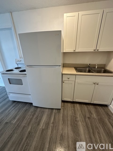 A white fridge and stove in a kitchen with wooden flooring.