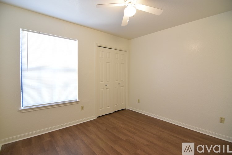 A room with a wooden floor, a ceiling fan, and a door.