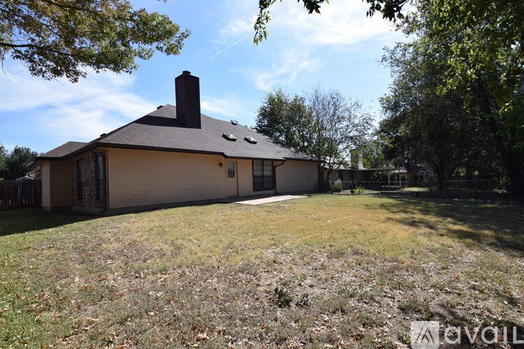 A house with a brown roof and a chimney is surrounded by trees and grass.