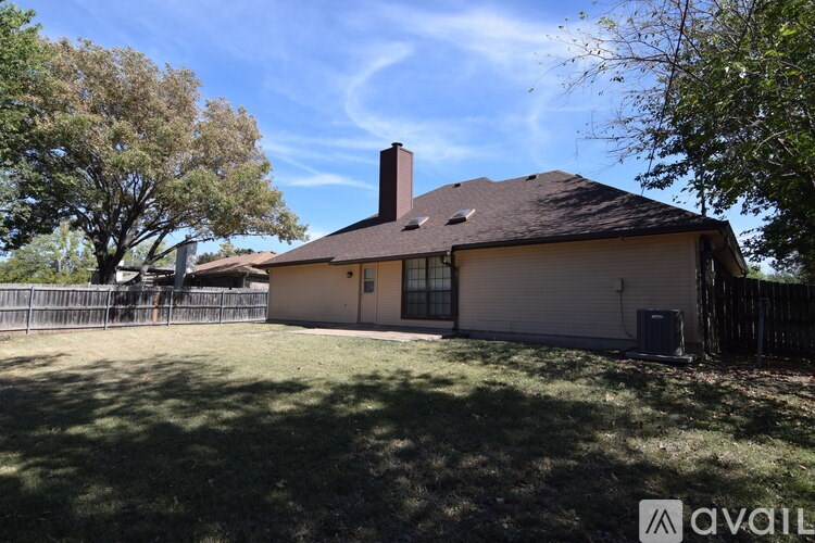 A house with a brown roof and a chimney is surrounded by a fence and trees.