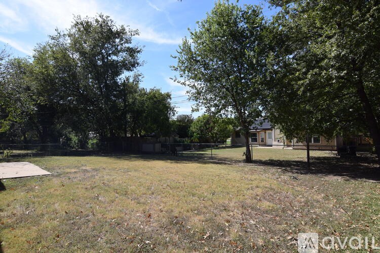 A grassy field with trees and a house in the background.