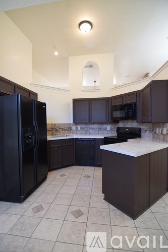 A kitchen with a black refrigerator and brown cabinets.