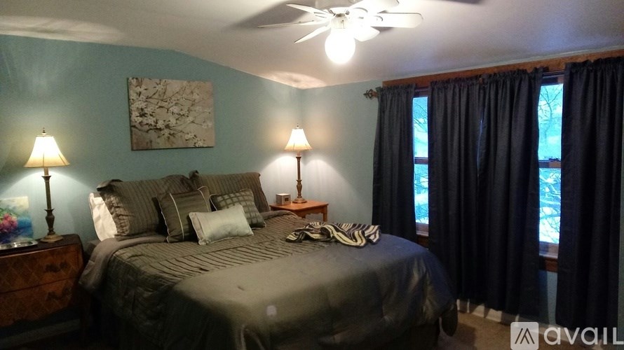 A bedroom with a bed, two lamps, and a ceiling fan.