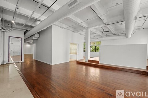 A spacious room with wooden floors and white walls, featuring a large window and a door.