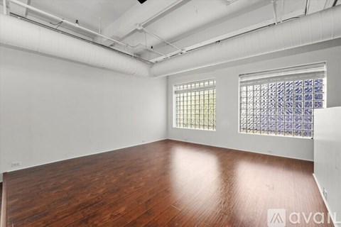 A room with wooden flooring and two windows.