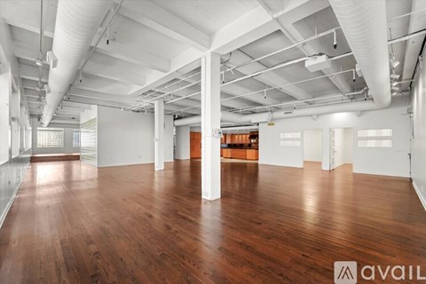 A spacious room with wooden floors and white walls, featuring a high ceiling with exposed pipes and ducts.