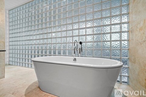 A white bathtub with a silver faucet is in front of a glass block wall.