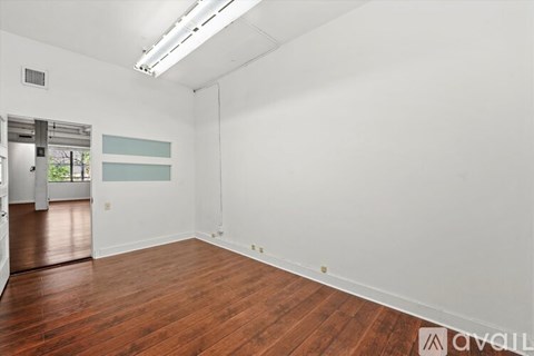A room with wooden flooring and white walls, with a door on the left side.