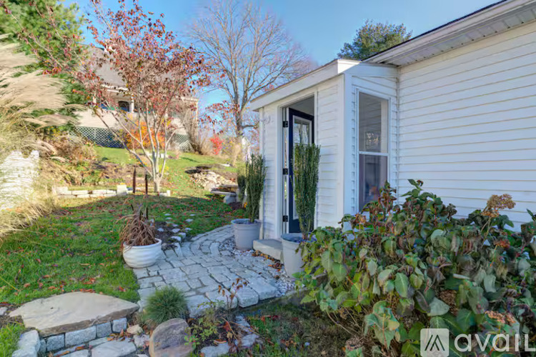 A house with a white siding and a black door is surrounded by a garden with a stone pathway.