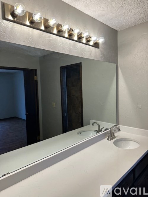 A bathroom with a white countertop and a mirror with lights above it.