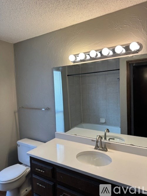 A bathroom with a white sink and a mirror with lights on it.