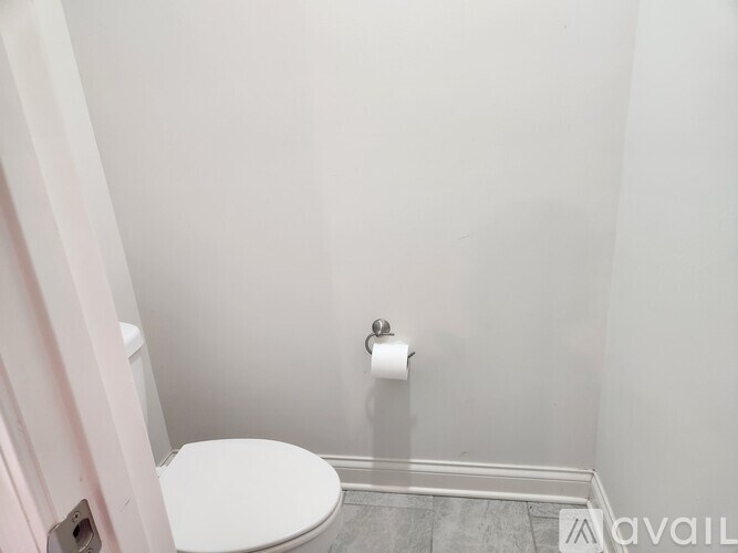 A white toilet in a small bathroom with a roll of toilet paper on the wall.