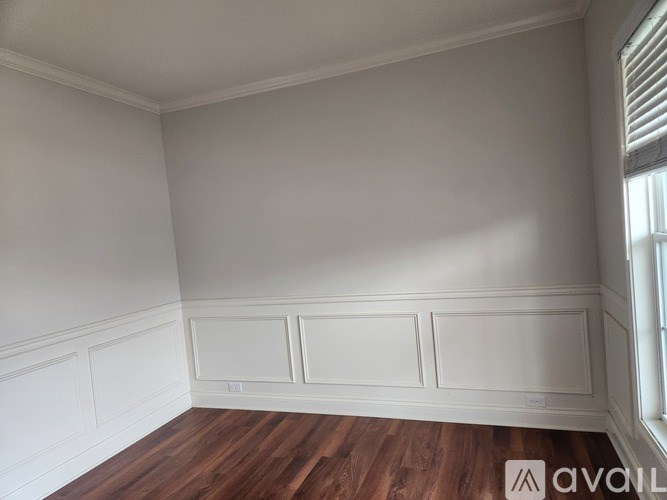 A room with white walls and wooden flooring with a window on the right side.