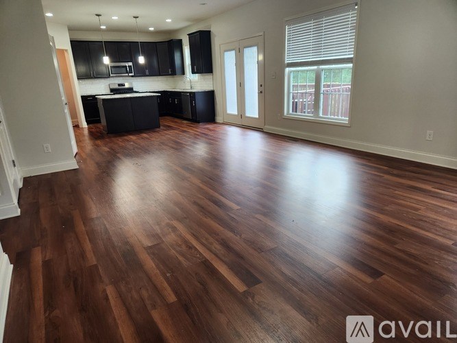 A spacious room with wooden flooring and a kitchen area.