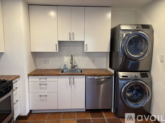 A modern kitchen with white cabinets and a washer and dryer stacked together.