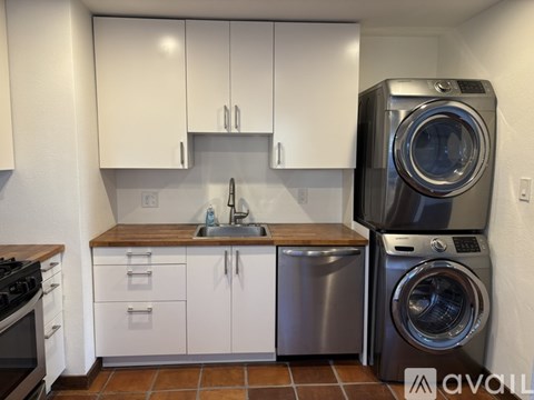 A modern kitchen with white cabinets and a washer and dryer stacked together.