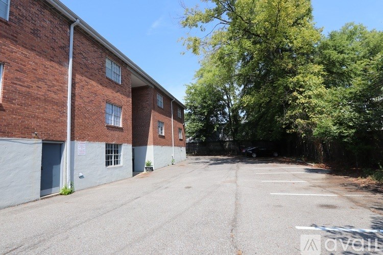A parking lot in front of a brick building with trees in the background.