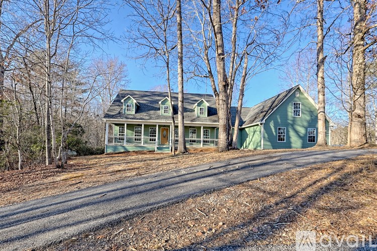 A green house with a porch is surrounded by bare trees.
