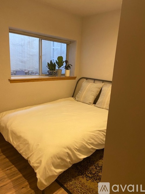 A bedroom with a bed, pillows, and a window with plants on the windowsill.